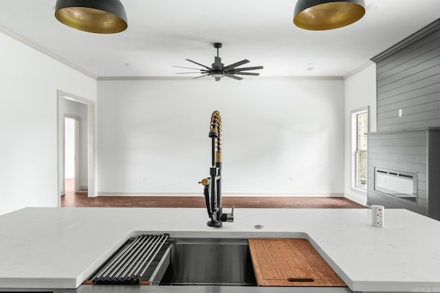 kitchen featuring light stone counters, ceiling fan, ornamental molding, and a sink