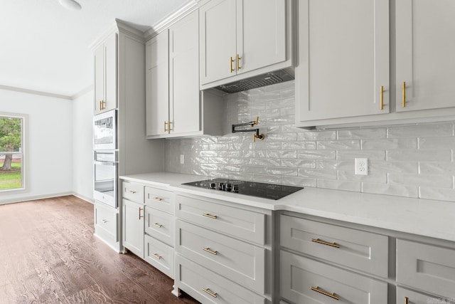 kitchen featuring light countertops, black electric cooktop, backsplash, stainless steel oven, and dark wood-type flooring