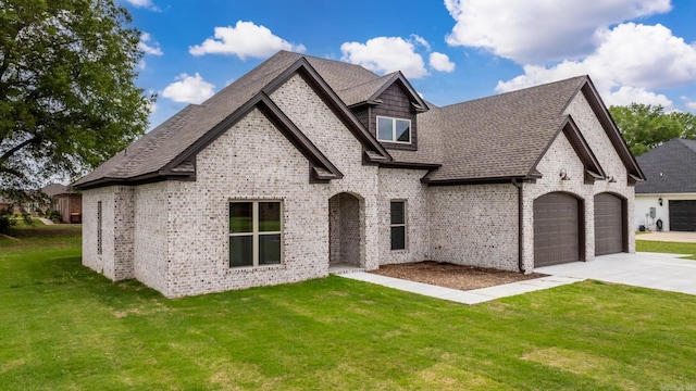 french country style house featuring a front yard, driveway, an attached garage, and brick siding