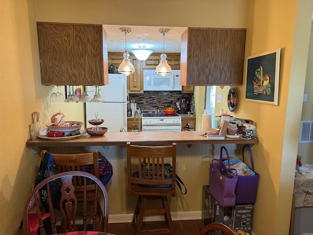 kitchen with a breakfast bar, tasteful backsplash, a sink, white appliances, and a peninsula