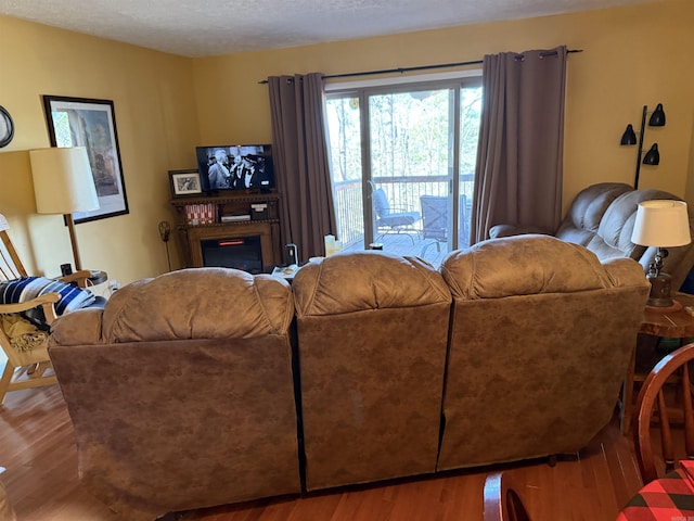 living area featuring a textured ceiling, wood finished floors, and a glass covered fireplace