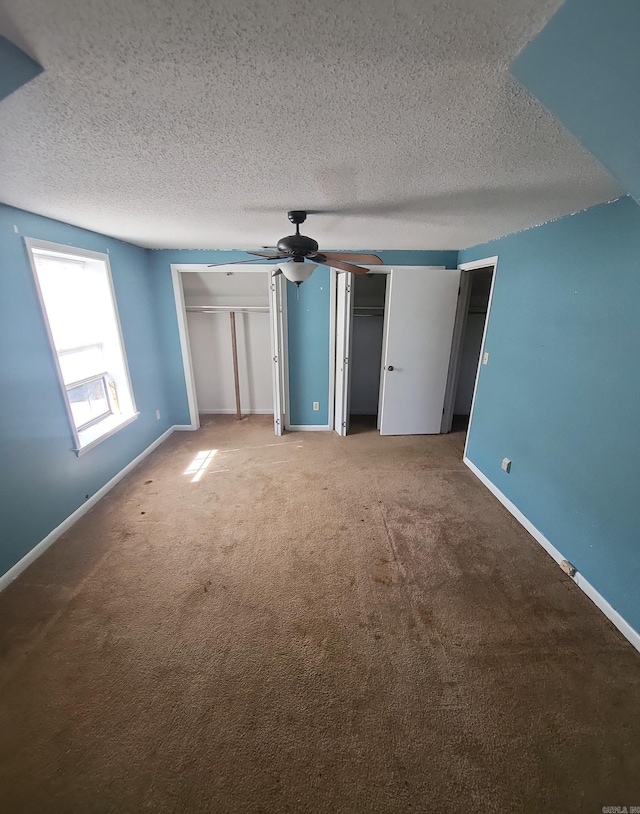 unfurnished bedroom featuring carpet floors, two closets, a ceiling fan, a textured ceiling, and baseboards