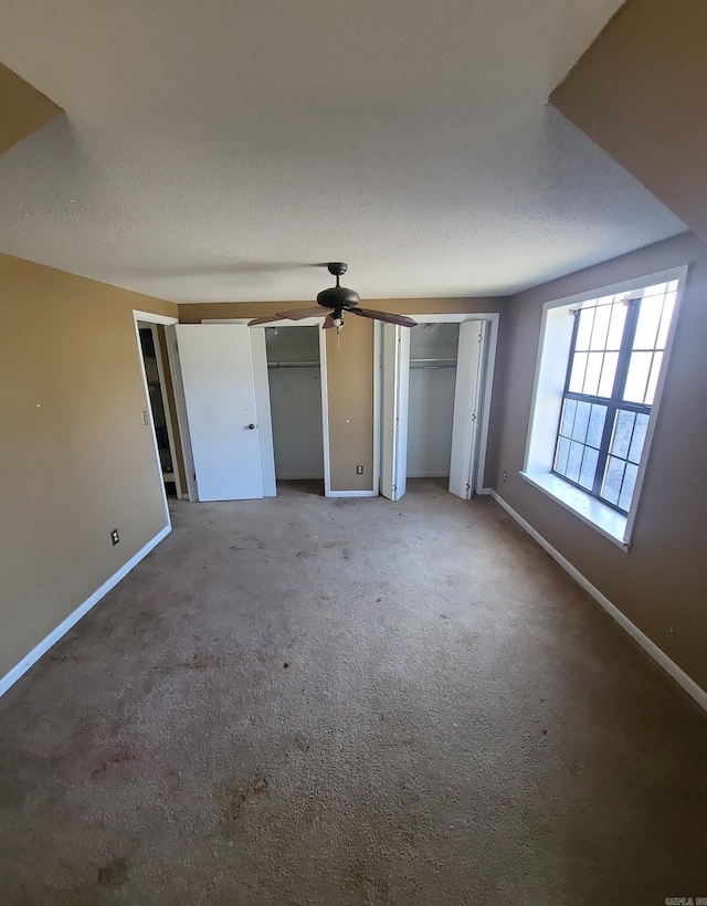 unfurnished bedroom featuring multiple closets, a textured ceiling, and baseboards