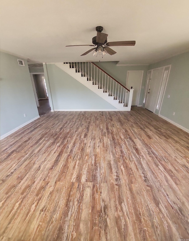 unfurnished living room with visible vents, ceiling fan, stairway, and wood finished floors