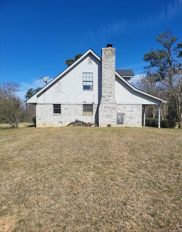 view of side of home with a chimney, a lawn, and brick siding