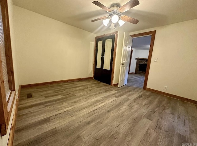 spare room with baseboards, visible vents, ceiling fan, wood finished floors, and a fireplace