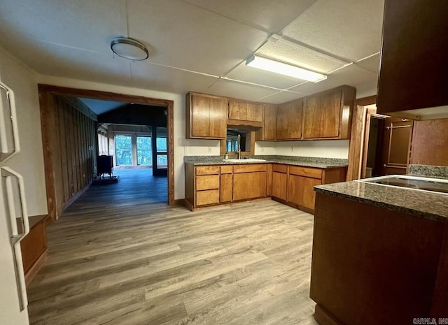 kitchen with baseboards, brown cabinets, a sink, and light wood finished floors