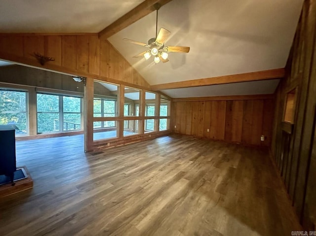 unfurnished living room featuring vaulted ceiling with beams, ceiling fan, wood finished floors, and wooden walls