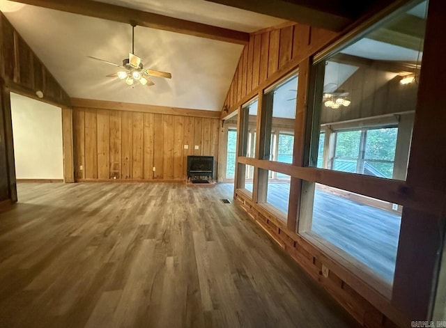 unfurnished living room with vaulted ceiling with beams, visible vents, a ceiling fan, wood walls, and wood finished floors