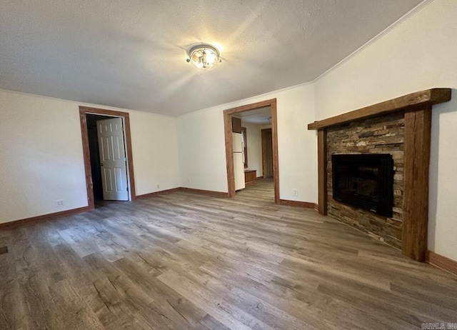 unfurnished living room featuring a textured ceiling, a stone fireplace, wood finished floors, and baseboards