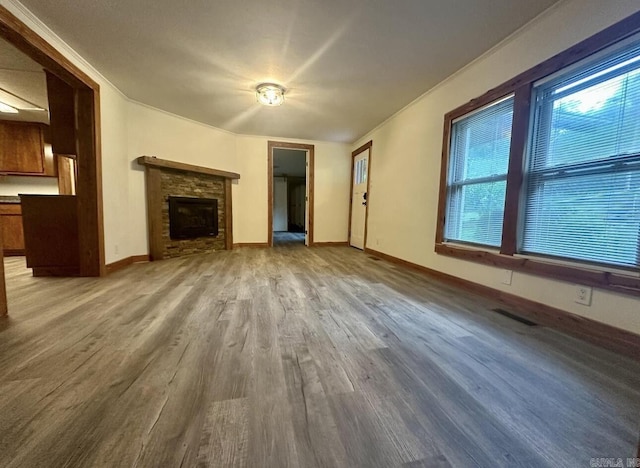 unfurnished living room with crown molding, a fireplace, visible vents, wood finished floors, and baseboards