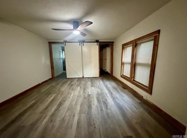 unfurnished bedroom featuring a ceiling fan, wood finished floors, baseboards, and a barn door