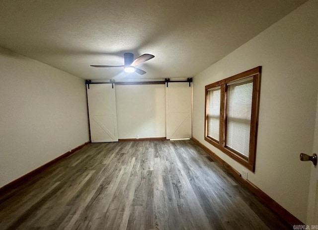 spare room with a barn door, a textured ceiling, a ceiling fan, and wood finished floors