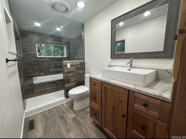 full bath featuring toilet, visible vents, a tile shower, and wood finished floors