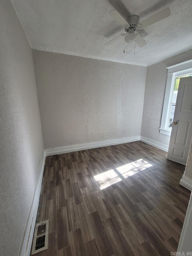 spare room featuring visible vents, baseboards, dark wood finished floors, and a textured wall