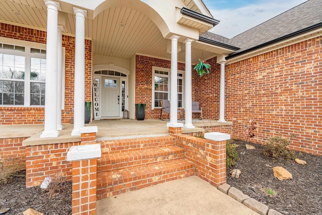 entrance to property with a porch, brick siding, and roof with shingles