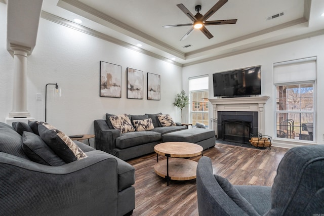 living room with dark wood-style floors, a tray ceiling, visible vents, and decorative columns