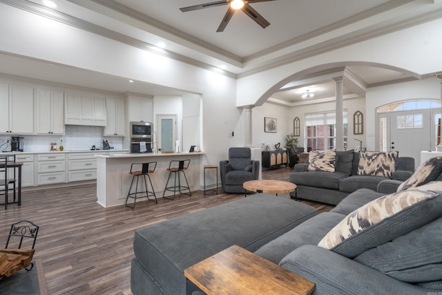 living room with arched walkways, dark wood-type flooring, ornamental molding, a ceiling fan, and ornate columns