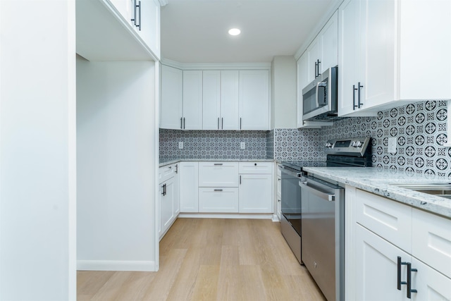 kitchen featuring light wood-style flooring, white cabinets, appliances with stainless steel finishes, backsplash, and light stone countertops