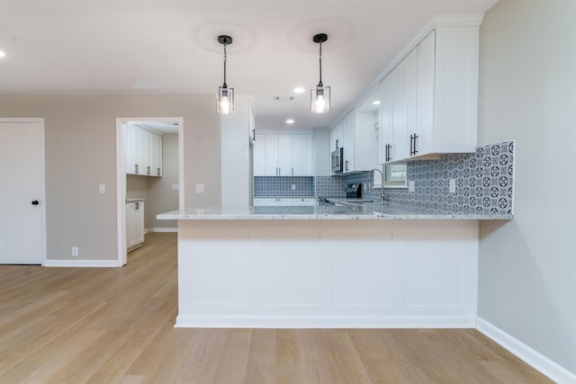 kitchen featuring tasteful backsplash, stainless steel microwave, light wood-style floors, light stone countertops, and a peninsula