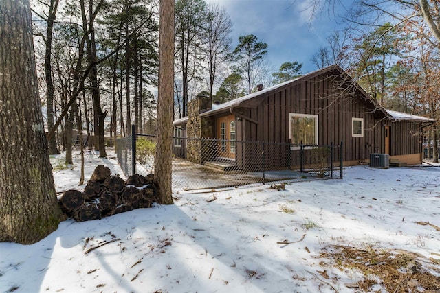 view of snowy exterior with board and batten siding, fence, a chimney, and central air condition unit