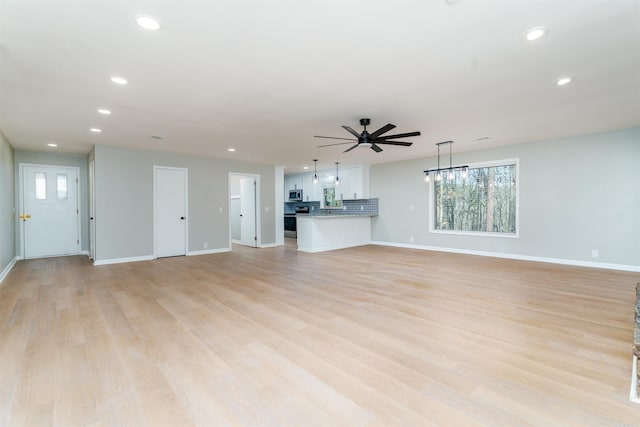 unfurnished living room featuring recessed lighting, light wood-style flooring, baseboards, and ceiling fan with notable chandelier