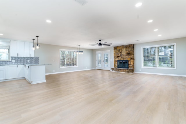 unfurnished living room featuring a healthy amount of sunlight, light wood finished floors, a ceiling fan, and a stone fireplace