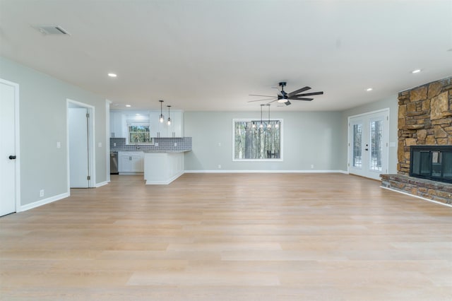 unfurnished living room featuring ceiling fan, a stone fireplace, visible vents, baseboards, and light wood-type flooring