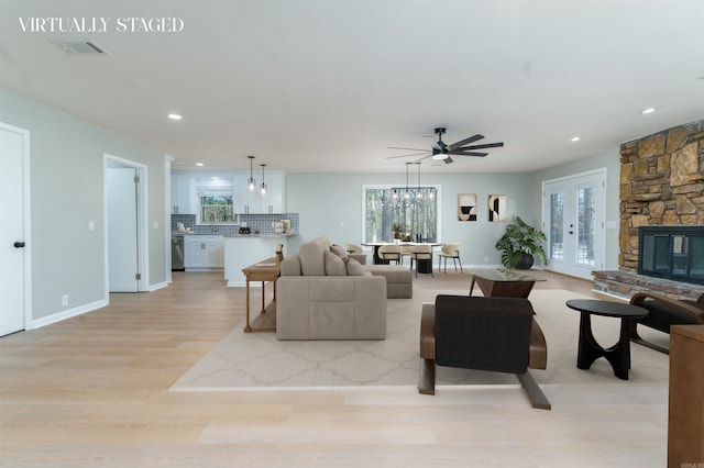 living area with light wood finished floors, baseboards, visible vents, a stone fireplace, and french doors