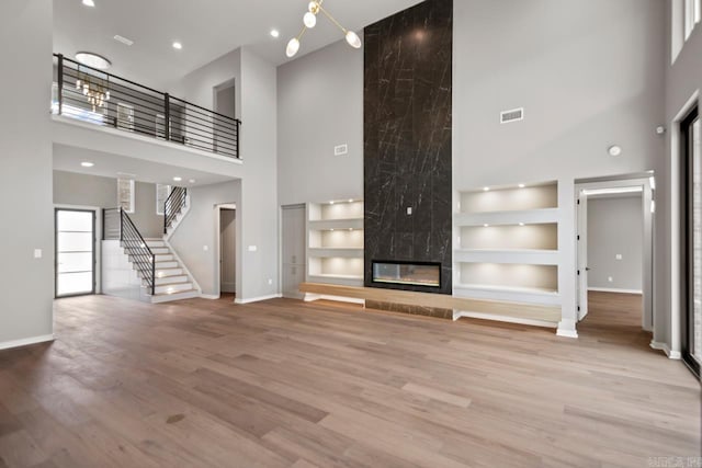 unfurnished living room featuring a high ceiling, wood finished floors, a high end fireplace, visible vents, and built in features