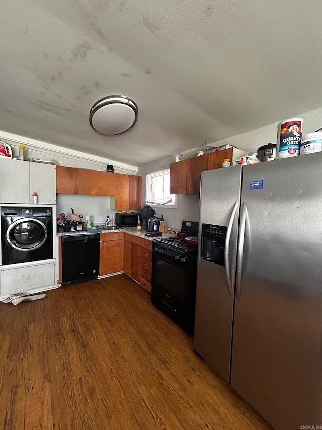 kitchen featuring washer / dryer, dark wood finished floors, brown cabinets, black appliances, and a sink