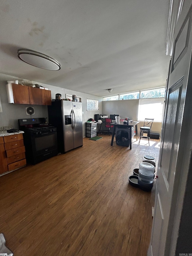 kitchen featuring brown cabinetry, stainless steel fridge with ice dispenser, black gas range oven, dark wood-type flooring, and light countertops