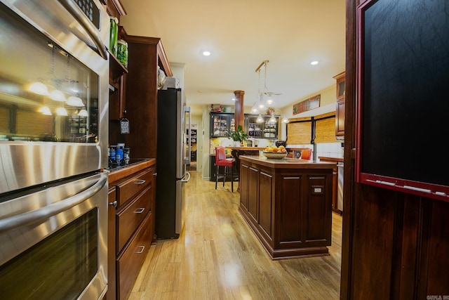 kitchen with reddish brown cabinets, a center island, pendant lighting, appliances with stainless steel finishes, and light wood-type flooring