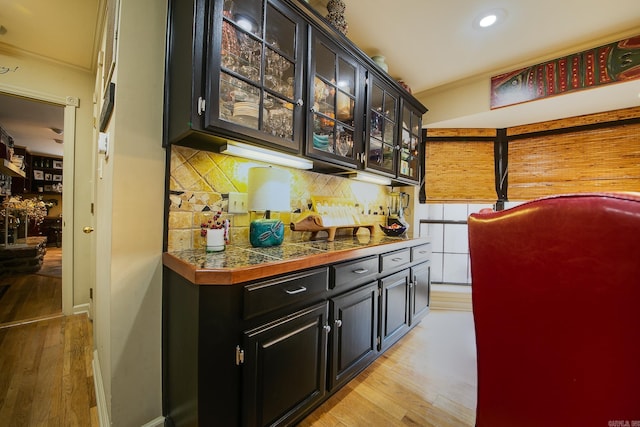 bar with baseboards, light wood-style floors, backsplash, and crown molding