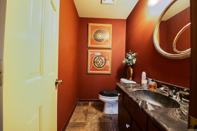 bathroom featuring a textured ceiling, vanity, toilet, and baseboards