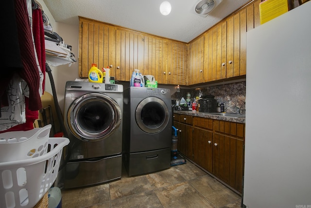 laundry area with a textured ceiling, washing machine and dryer, a sink, visible vents, and cabinet space