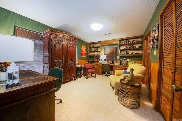 office with light carpet, wooden walls, visible vents, a wainscoted wall, and a textured ceiling