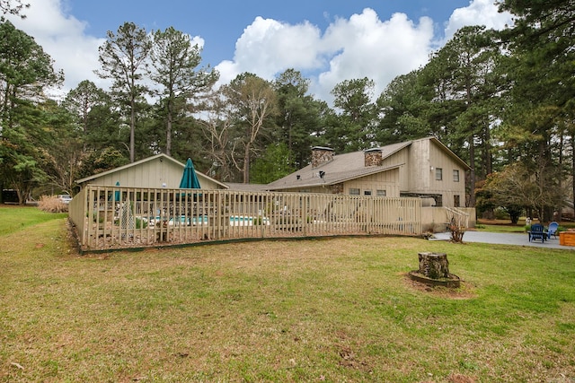 rear view of property featuring a lawn, a chimney, fence, and a fenced in pool