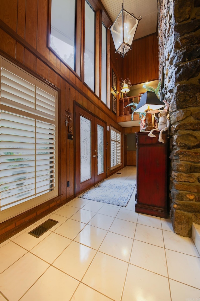 foyer with wooden walls, visible vents, tile patterned floors, french doors, and a notable chandelier