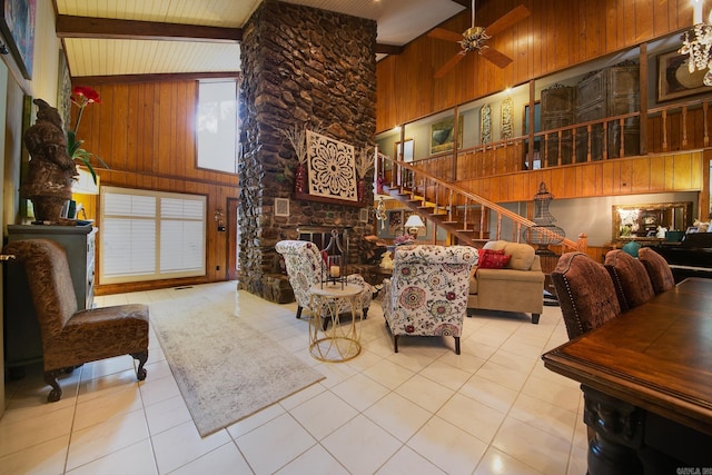 tiled living area featuring beam ceiling, wooden walls, a stone fireplace, high vaulted ceiling, and stairs