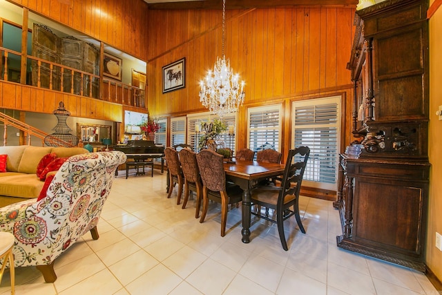 dining area featuring light tile patterned floors, an inviting chandelier, a towering ceiling, and wooden walls