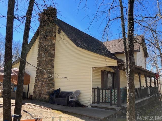 view of side of home featuring covered porch, roof with shingles, and a chimney