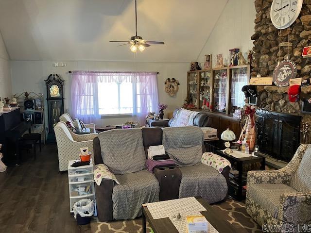 living room featuring ceiling fan, vaulted ceiling, wood finished floors, and a stone fireplace