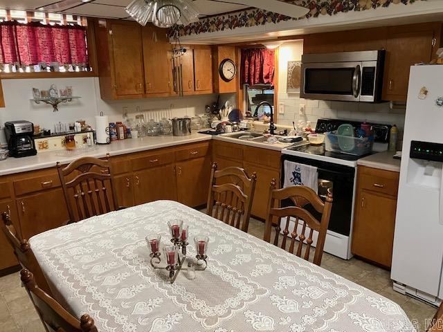 kitchen featuring white refrigerator with ice dispenser, light countertops, stainless steel microwave, electric range, and brown cabinetry