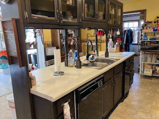 kitchen featuring a sink, light countertops, dark brown cabinets, dishwasher, and glass insert cabinets