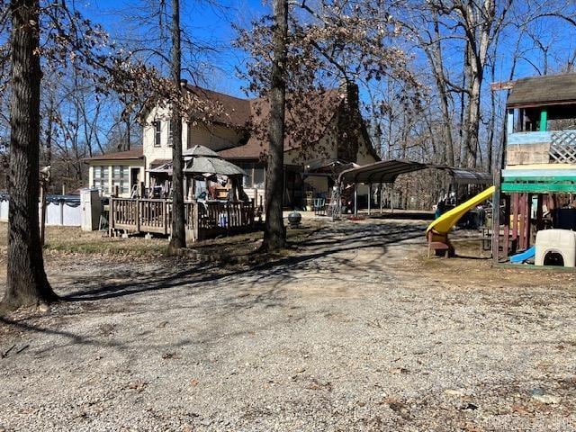 exterior space featuring dirt driveway, playground community, and a detached carport