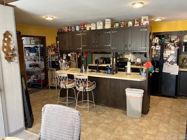 kitchen featuring dark brown cabinetry, light countertops, black fridge, and a kitchen breakfast bar