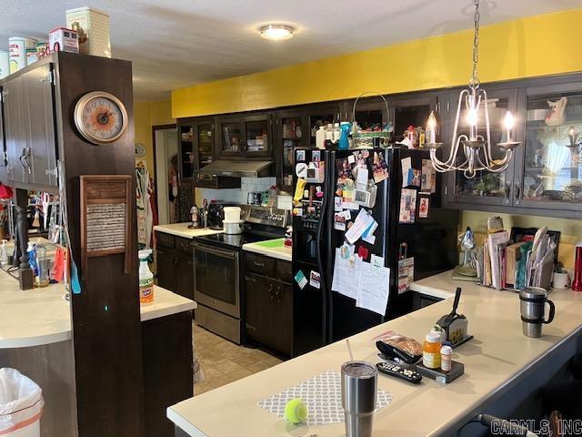 kitchen with electric range, an inviting chandelier, light countertops, under cabinet range hood, and black fridge