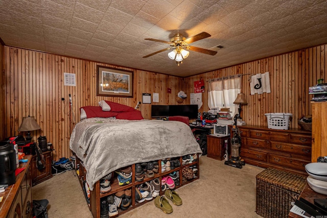 carpeted bedroom with wood walls, visible vents, and a ceiling fan