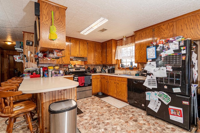 kitchen with under cabinet range hood, black dishwasher, wooden walls, and electric stove